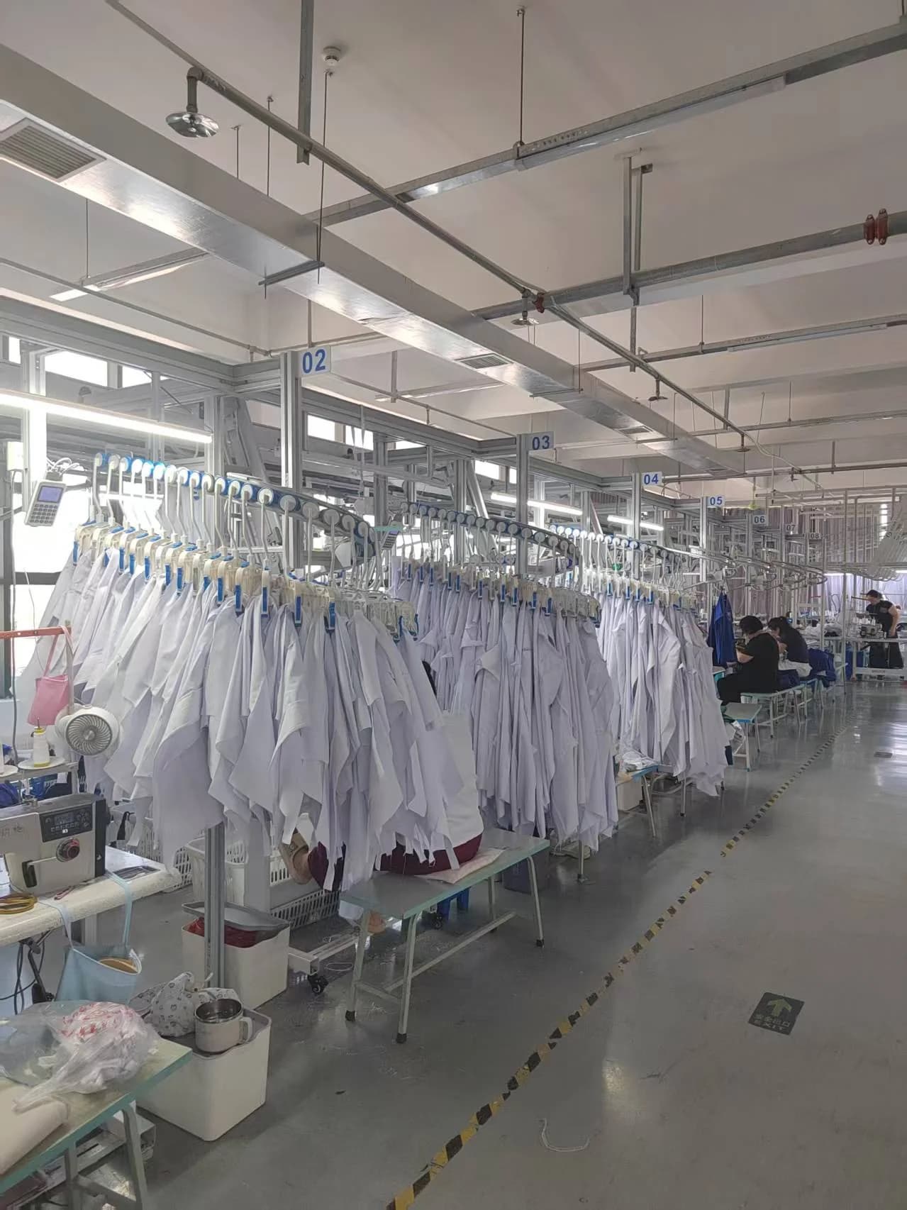 White garments on the overhead rail alongside sewing workstations